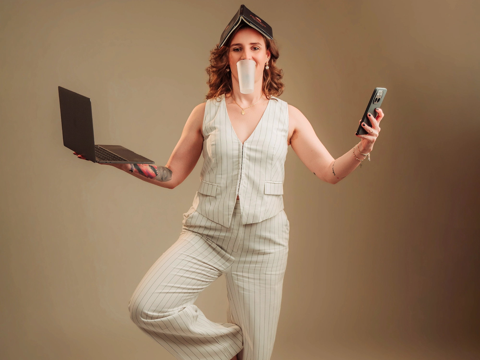 Uma fotografia divertida da Ana, a segurar um portátil, um telefone, um copo e um livro na cabeça, tudo ao mesmo tempo.