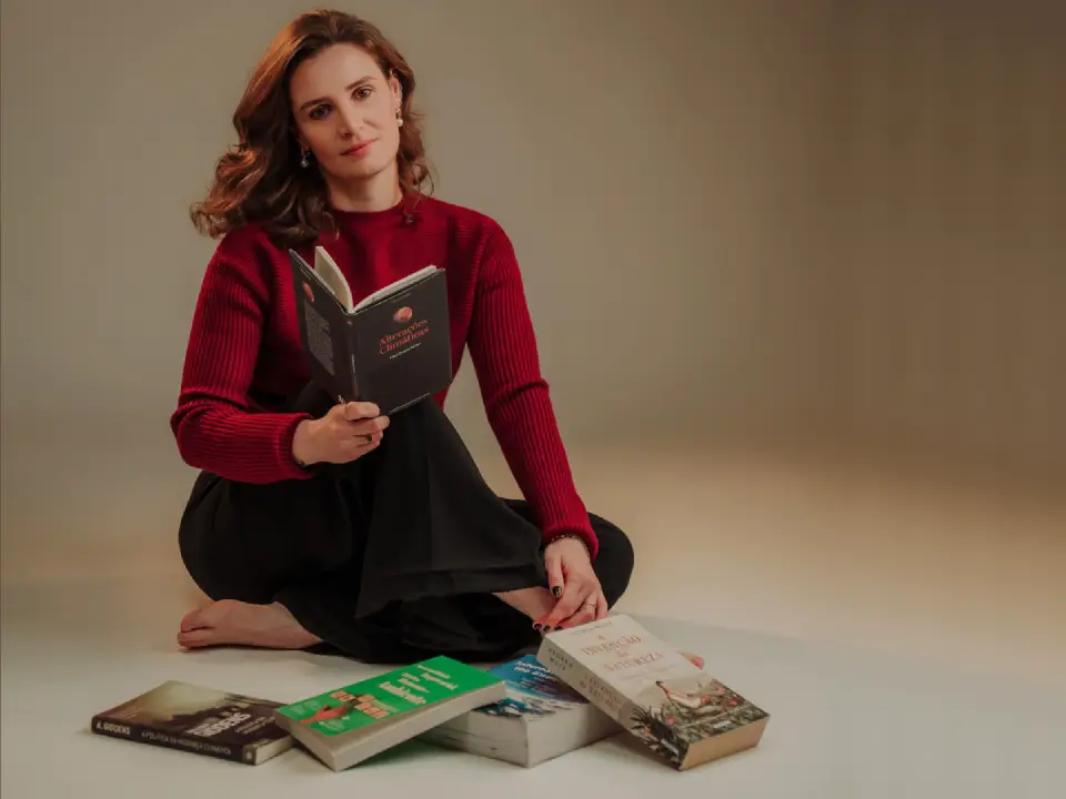 Ana segura um livro sentada no chão, onde outros quatro se encontram espalhados.